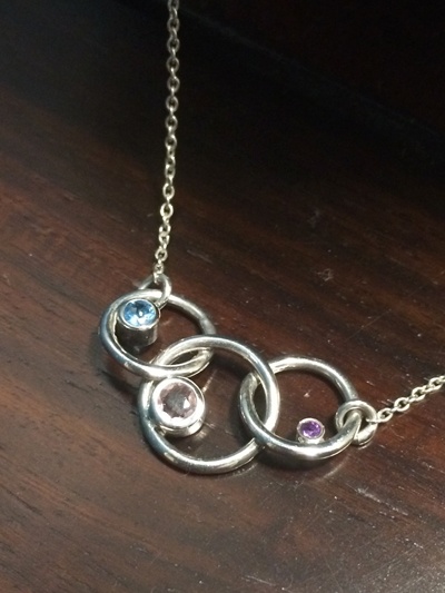 The Final Piece. Three linked silver hoops with birthstones, representing mother and children.
